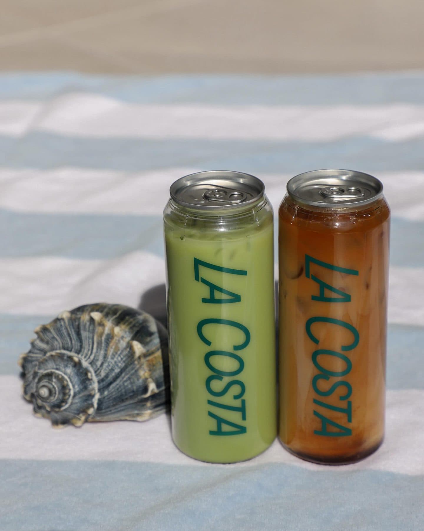 Two La Costa cans and a seashell on a striped beach towel