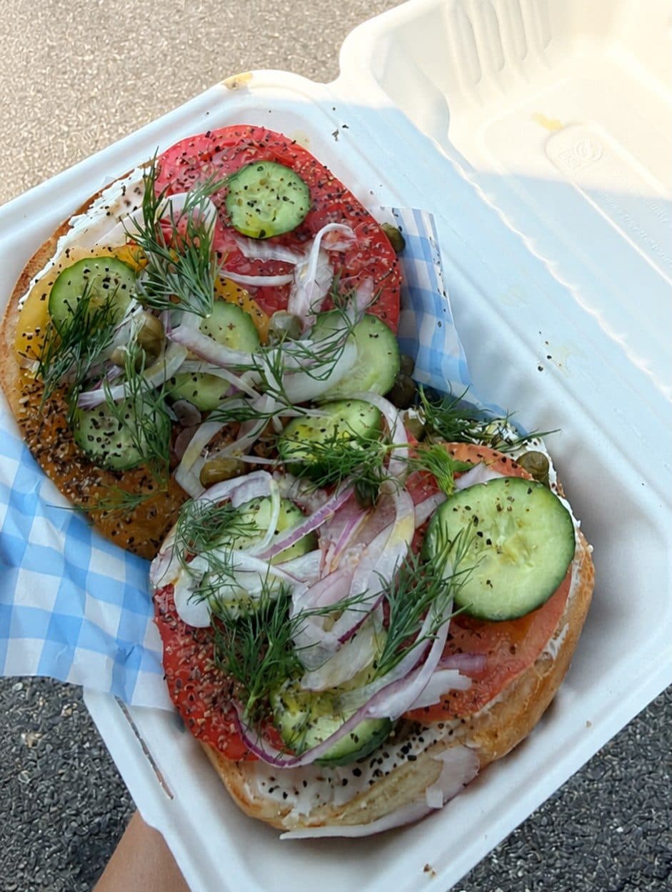 The Lox Special open in its takeout box with cucumber, red onion and dill