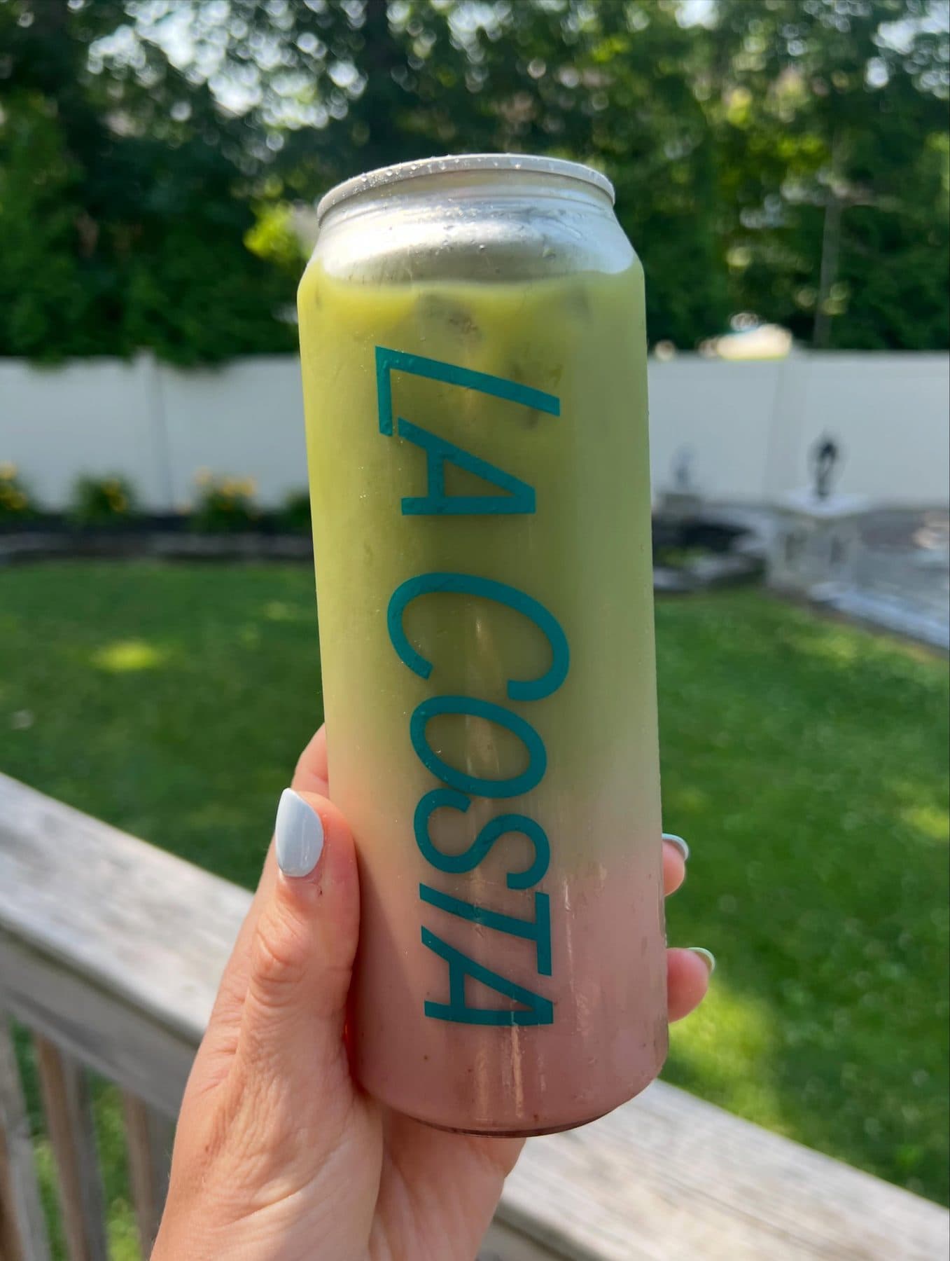 A hand holding a La Costa matcha can on a sunny back deck