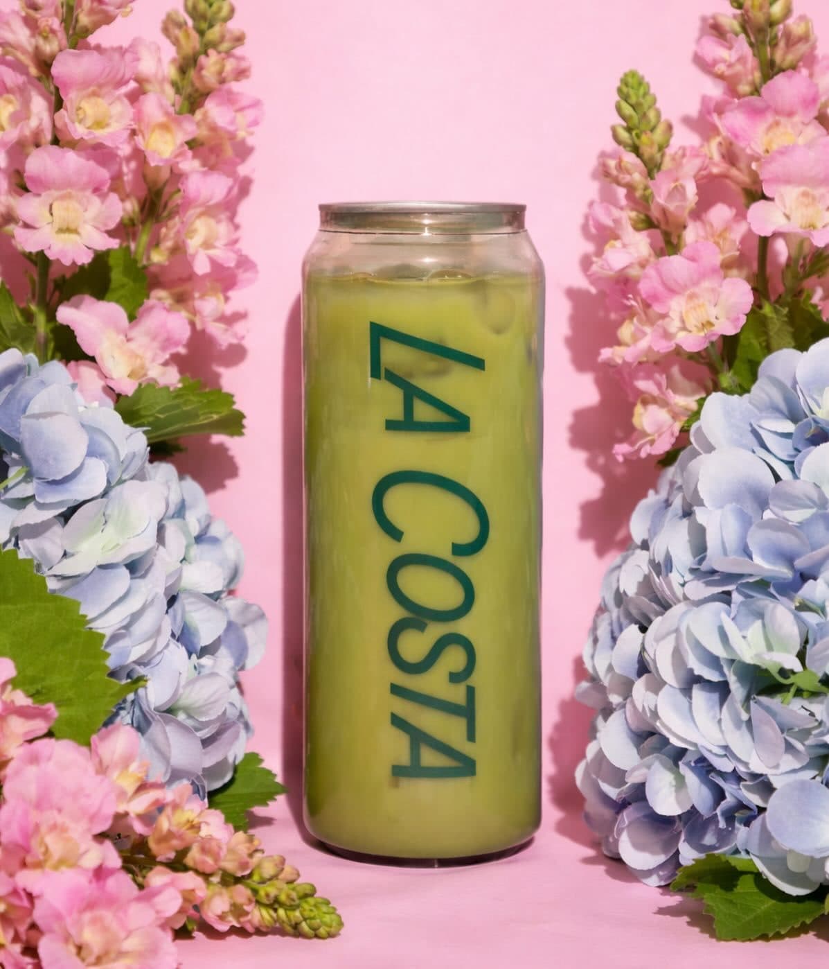 A La Costa matcha can standing between pink snapdragons and blue hydrangeas