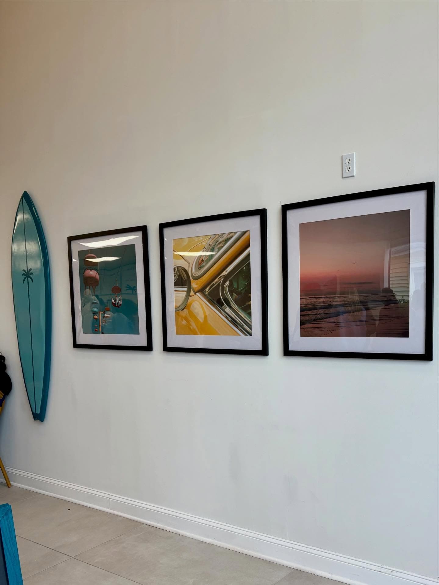 The teal palm surfboard hung beside three framed prints on the shop wall